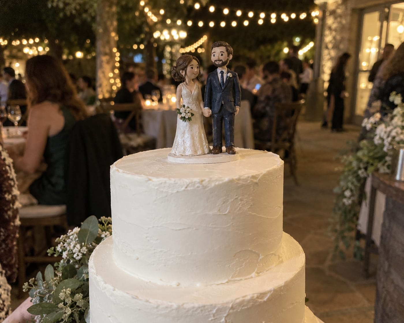 A hand-painted bride and groom cake topper on a white wedding cake